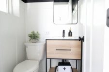 a small and chic modern powder room with black walls and white paneling, a black and white floor, a timber vanity and white appliances