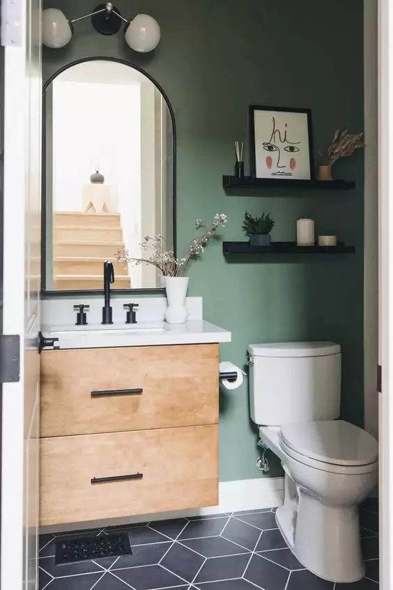 a small and cool modern farmhouse powder room with a green accent wall, a timber floating vanity, a curved mirror and open shelves
