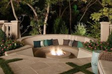 a small and cozy modern outdoor sunken fire put with a built-in bench, lots of pillows and blooms and a fire pit itself