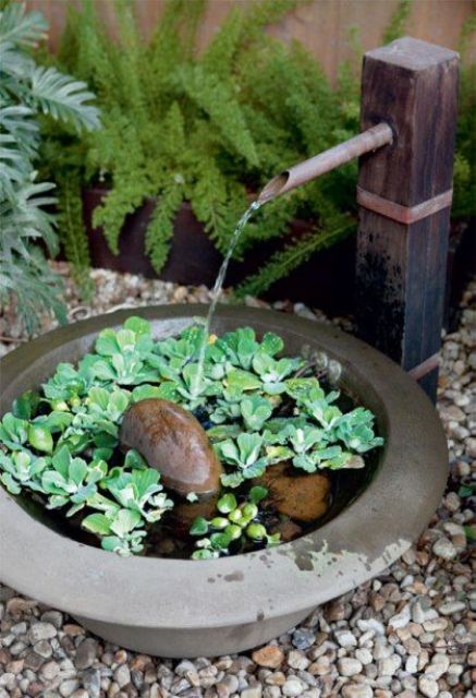 a small fountain inspired by traditional bamboo Japanese ones, with a concrete bowl, rocks and some water plants