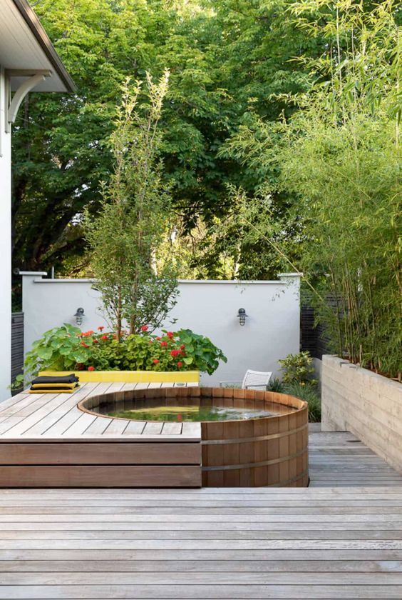 a small laconic wooden deck with a round hot tub and some greenery and blooms around is a cool idea for outdoors