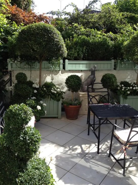 a small townhouse garden with potted greenery and a tree, blooms in wooden crates and vintage garden furniture