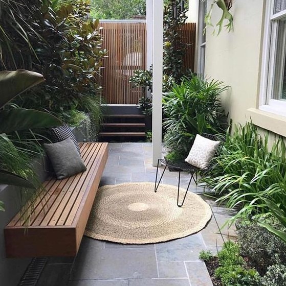 a small townhouse garden with stone tiles, a built in bench, hairpin leg furniture and potted greenery with much texture