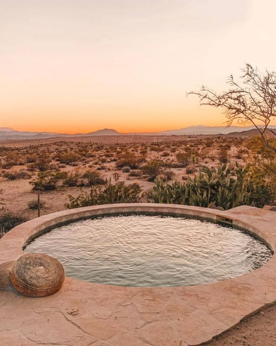 a small yet elegant neutral round pool of stone and tiles, with a stone deck around it and a view of the desert to enjoy