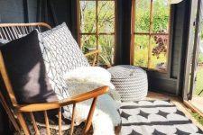 a small yet lovely modern she shed with a wooden daybed with pillows, potted greenery, a pouf and a printed rug