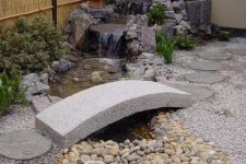 a small yet very chic front yard Japanese garden with a stream with rocks and a stone bridge and greenery is fabulous