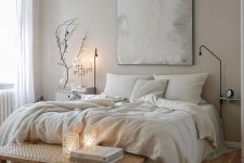 a soothing and relaxing greige bedroom with a bed with creamy bedding, a woven bench, a catchy chandelier and some neutral textiles