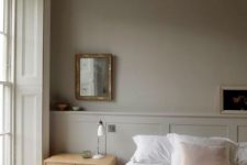 a soothing greige bedroom with a grey ceiling and paneling, a bed with neutral bedding, a light-stained nightstand, a mirror and shutters