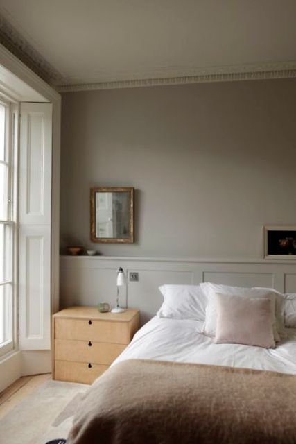 a soothing greige bedroom with a grey ceiling and paneling, a bed with neutral bedding, a light-stained nightstand, a mirror and shutters