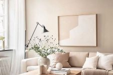 a soothing greige living room with a beige sofa, some pillows, an artwork, a coffee table and a black floor lamp