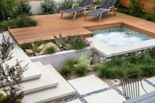 a stylish modern backyard with a wooden deck, stone tiles and pebbles, steps, cool furniture and plants and a built-in hot bathtub