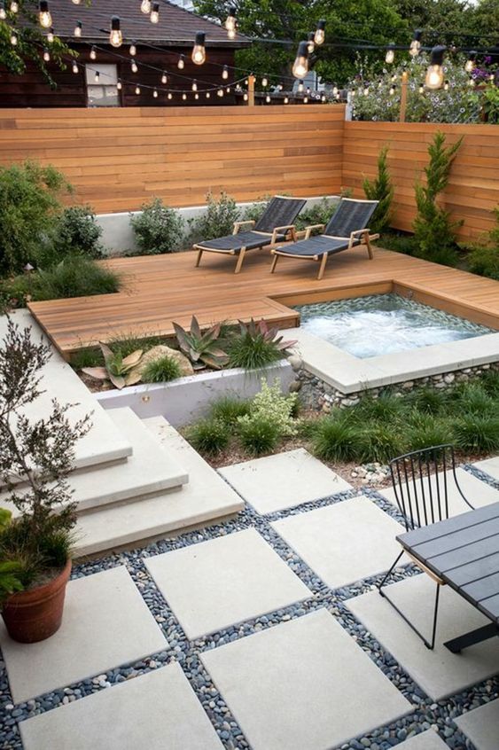 a stylish modern backyard with a wooden deck, stone tiles and pebbles, steps, cool furniture and plants and a built in hot bathtub