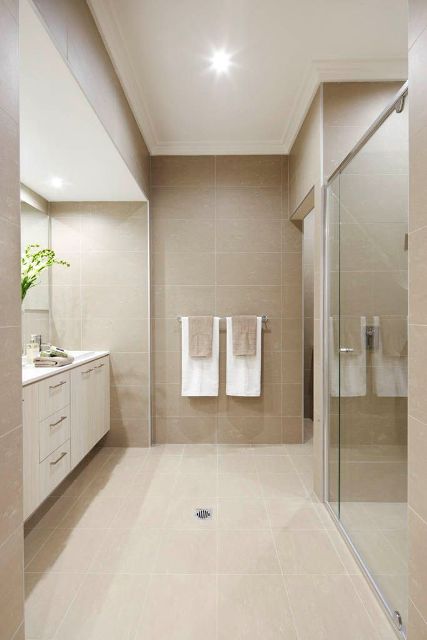 a stylish modern bathroom done with large scale greige tiles, a white built-in vanity, a glass-enclosed shower and a large mirror