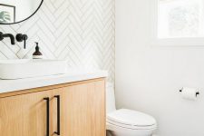 a stylish modern farmhouse powder room with a herringbone tile accent wall, a floating vanity, a black hex tile floor