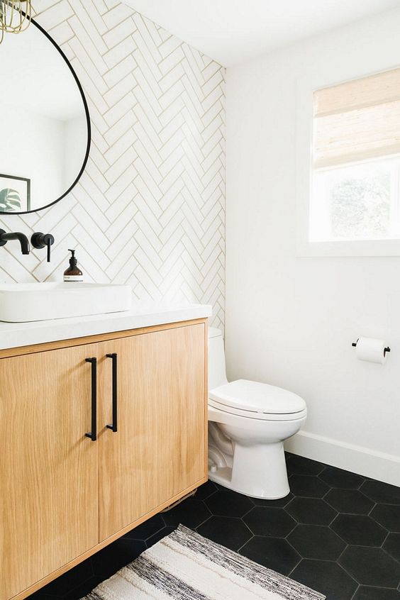 a stylish modern farmhouse powder room with a herringbone tile accent wall, a floating vanity, a black hex tile floor