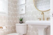 a stylish neutral powder room with printed wallpaper, a round mirror in a gilded frame, a free-standing sink and some plants