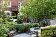 a stylish townhouse garden with a stone platform, a fire pit, a green sofa, planted flowers and greenery