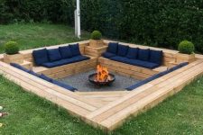 a sunken patio built of wood, with navy upholstery, greenery and a fire pit in the center is a cool and cozy idea
