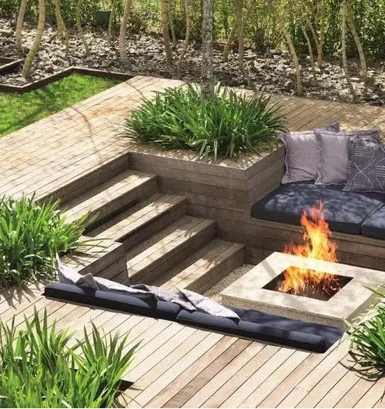 a sunken patio with a deck, a fire pit, built-in benches with pillows and grasses growing around is a very lovely space