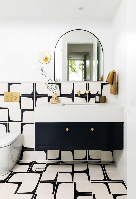 a super chic modern powder room in black and white, with a black vanity and a neutral sink, gold touches and a curved mirror for more chic