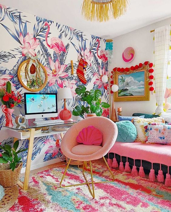 a super colorful and fun home office with a floral accent wall, a pink sofa with bright pillows, a pink chair, a bright rug and colorful art