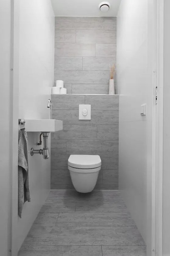 a tiny contemporary powder room wiht grey and white tiles, a wall-mounted sink and a toilet plus lights