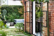 a townhouse courtyard with a stone tile walkway, greenery, potted plants, a living wall and some outdoor furniture