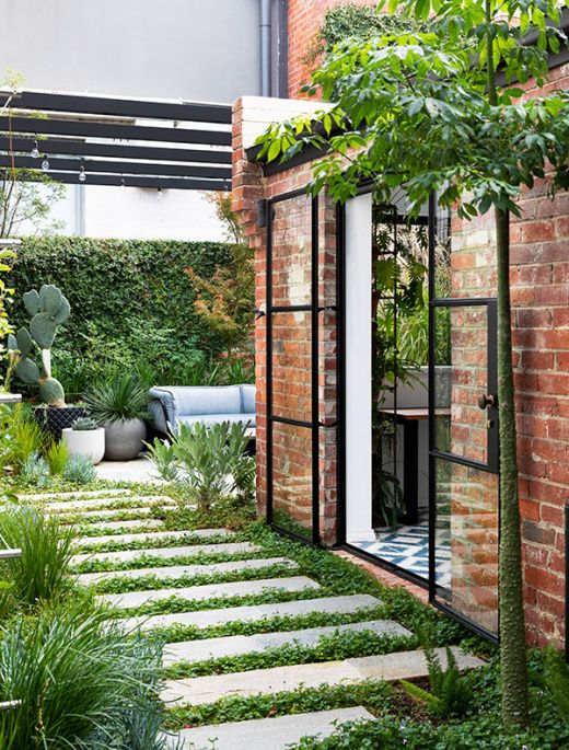 a townhouse courtyard with a stone tile walkway, greenery, potted plants, a living wall and some outdoor furniture