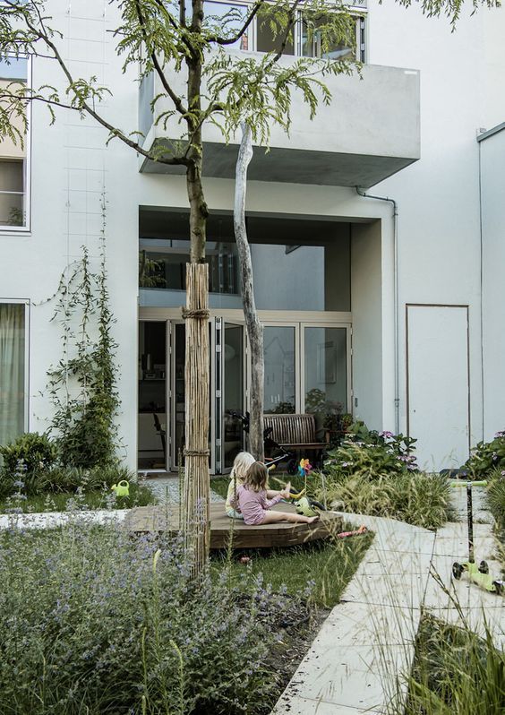 a townhouse courtyard with green lawn, trees and shrubs, stone tile walkways and a wooden deck for kids to sit on