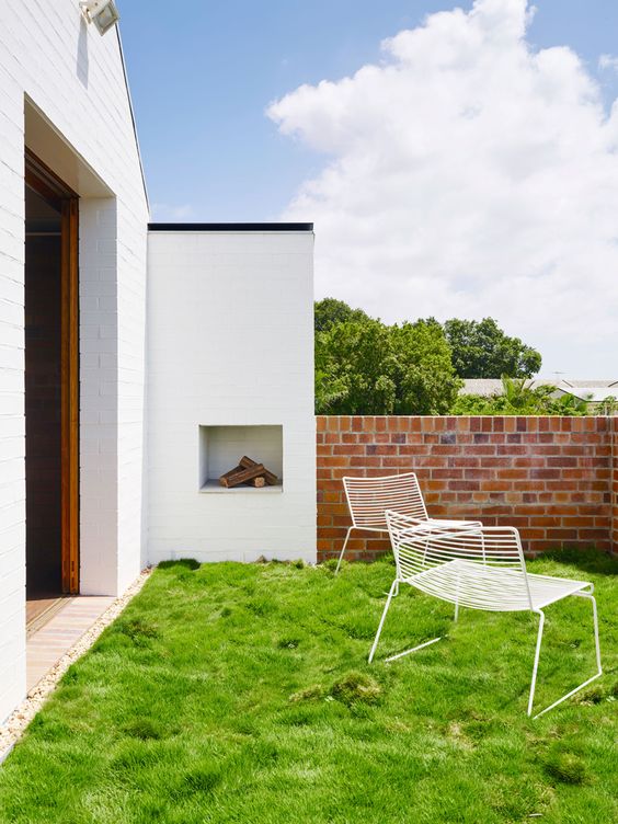 a townhouse courtyard with green lawn, white metal chairs and a built-in fireplace is a pretty and welcoming space