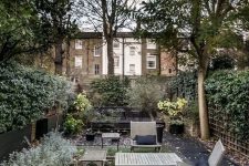 a townhouse garden with a lawn, shrubs and trees, simple wooden furniture and walls around for privacy