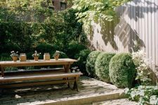 a townhouse garden with stone steps, greenery and boxwood growing and a simple wooden dining set with benches