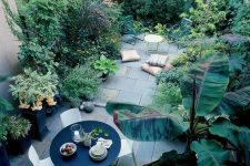a townhouse oasis with stone tiles, a contemporary dining set with a round table, growing greenery and plants and some pillows