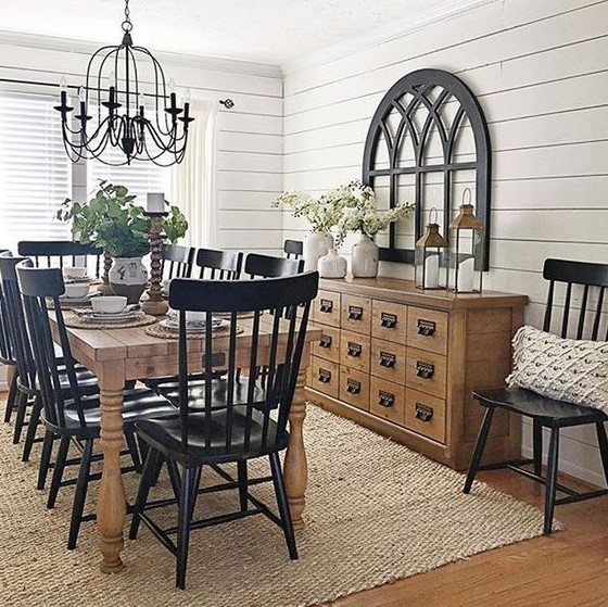 a traditional farmhouse dining space with black chairs, a light stained buffet and table, a metal chandelier