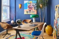 a vibrant home office with bold blue walls, colorful artworks and a rug, mismatching chairs and a statement plant in the corner