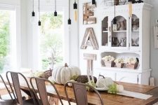 a vintage farmhouse dining room with a white buffet, a wooden sign, a ladder with bulbs, a wooden table and metal chairs