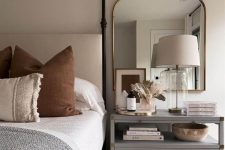 a vintage-inspired greige bedroom with a canopy bed with neutral and bold bedding, a grey nightstand that is a dresser and a large mirror