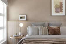 a welcoming greige bedroom with matching paneling, a bed with grey and greige bedding, a nightstand and some lights