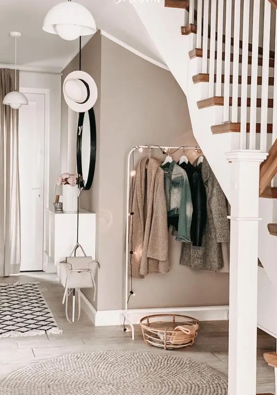 a welcoming greige entryway with a makeshift closet, a round mirror, a basket for storage, a white floating console table and pendant lamps