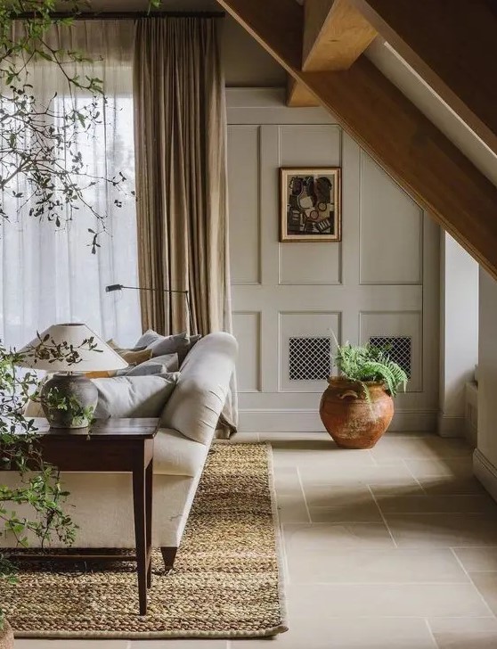 a welcoming greige living room with paneled walls, a neutral sofa, a dark stained coffee table, potted plants and a warm-colored rug