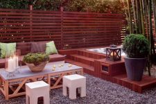 an above-ground hot tub with wood surround and steps in a cozy backyard with modern outdoor furniture, potted plants and bamboo