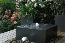 an edgy and ultra-modern black box fountain placed on rocks and with shiny metal spheres next to it