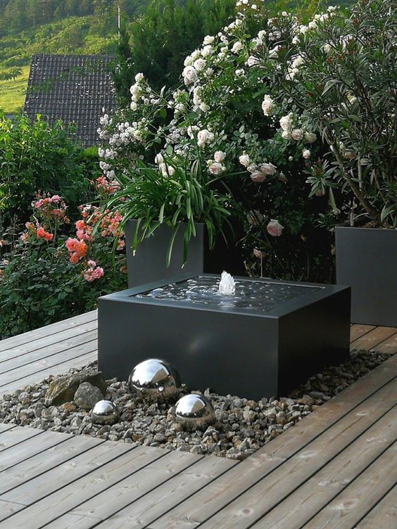 an edgy and ultra modern black box fountain placed on rocks and with shiny metal spheres next to it