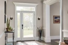 an elegant and lovely greige entryway with white frames and doors in white frames, a black console, artworks and umbrellas