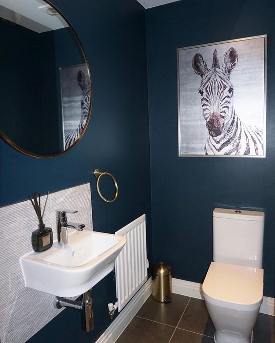 an elegant modern powder room with navy walls, neutral paneling, a round mirror, white appliances and a statement artwork