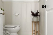 an elegant neutral modern powder room with creamy paneling and hex tiles on the floor, white appliances and dark foliage
