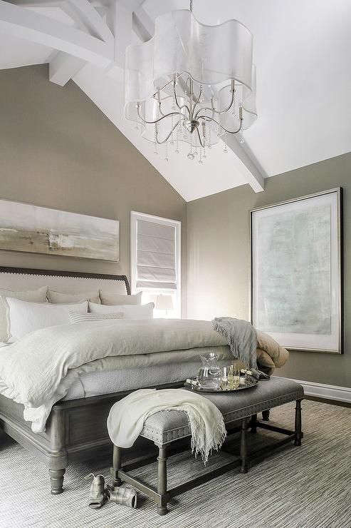 an exquisite greige bedroom with a grey vintage wooden bed wiht neutral bedding and a bench, a wave chandelier and artwork
