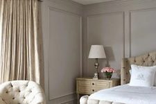 an exquisite greige bedroom with neutral upholstered furniture, a bench, neutral bedding, a crystal chandelier and tan printed curtains