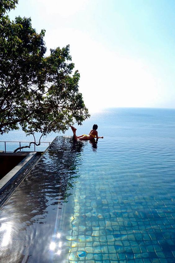 an infinity pool clad with mother of pearl green tiles, with a sea view and a tree next to the pool is awesome