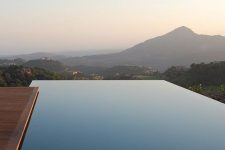 an infinity pool with a mountain view and a wooden deck compose a lovely minimalist outdoor space to have a rest in
